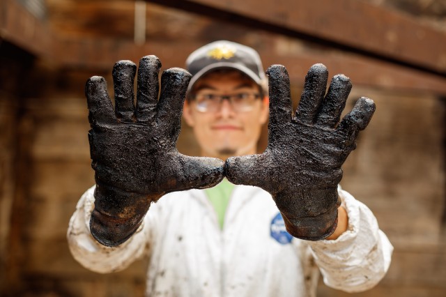 Photography of man with gloved hands entirely covered in &quot;tar&quot;