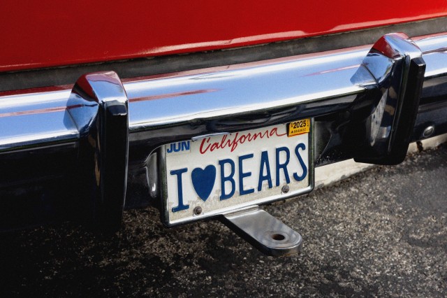 California license plate that reads &quot;I &#039;heart&#039; BEARS&quot; below a chrome bumper on the back end of a red car.