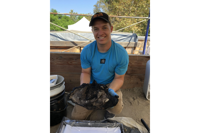 Sean Campbell outside, kneeling and holding up a fossil specimen