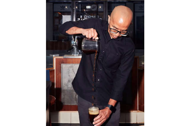 Coffee barista pouring coffee from a glass carafe held high, into a pint glass held low.
