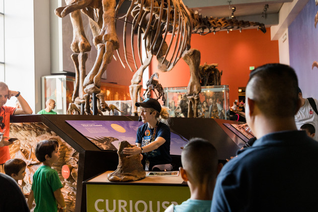 Visitors surrounding a Museum Educator standing at a cart with dinosaur foot specimen