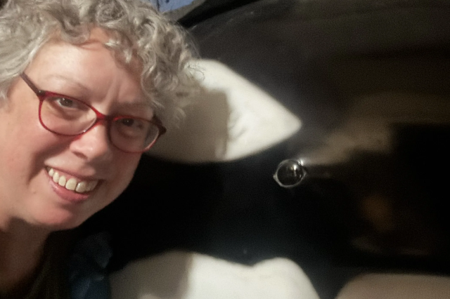 A woman with short gray hair and glasses next to a model orca