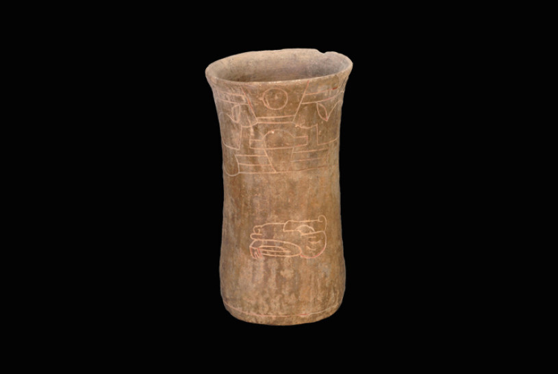 The photographed object is a Zapotec drinking cup from Oaxaca (200-300 B.C.) The object is a tall, cylindrical ceramic with a slightly flared rim and a gently cinched "waist" near the middle. It has an earthen, matte texture with a variegated color palette of sandy browns, muted ochre, and dark grey patches, suggesting age or exposure to minerals in the earth.