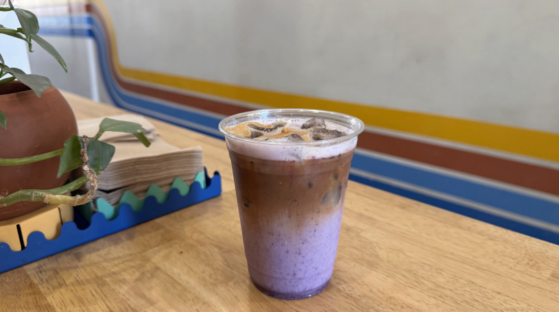 A brown and purple latte sits on the counter of Obet & Dels coffee shop with its iconic four stripes along the back wall.